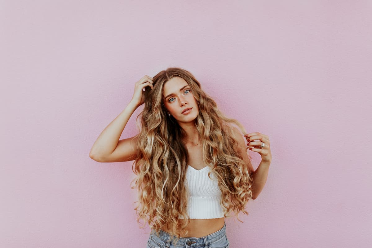 Šioje nuotraukoje mergina ilgais garbanotais plaukais rožiniame fone.